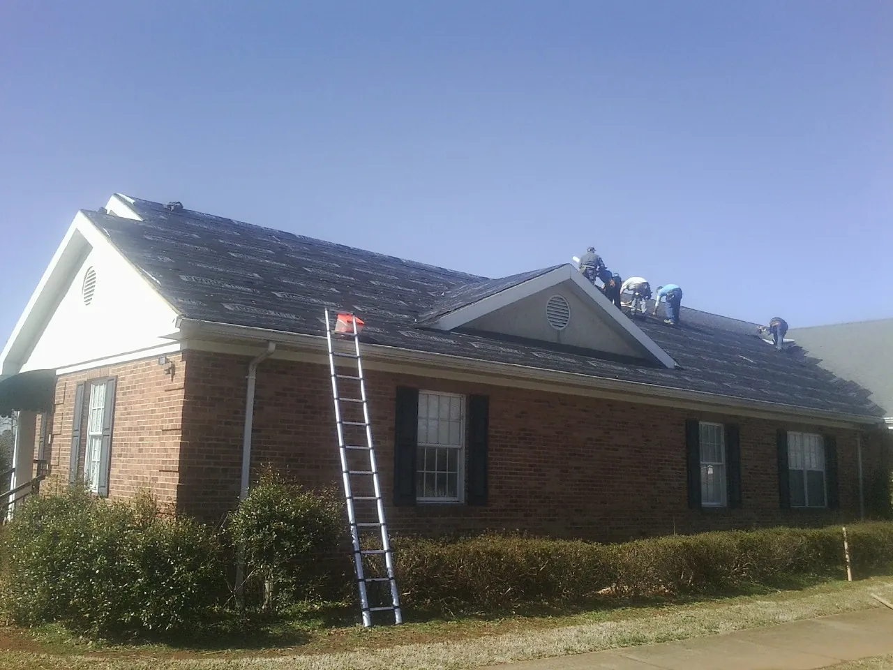 Crew tearing shingles off a brick ranch roof with a ladder set — Metal Roof Repair work by our crew in Alverton