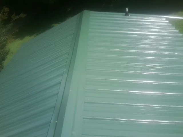 New green metal panels meeting at the ridge of a roof — Flat Roof Repair work by our crew in Alverton