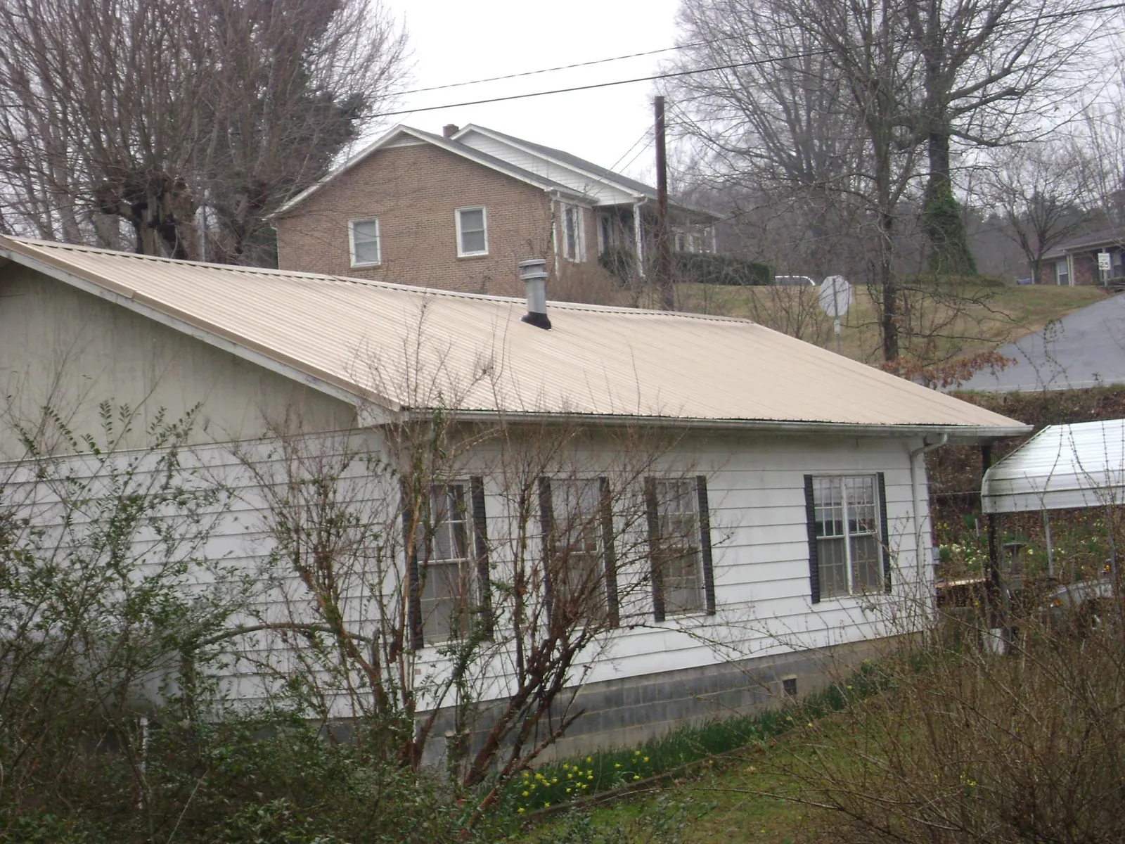 Tan metal roof on a white sided house set into a hillside — Commercial Roofing by Roofing Brothers in Alverton