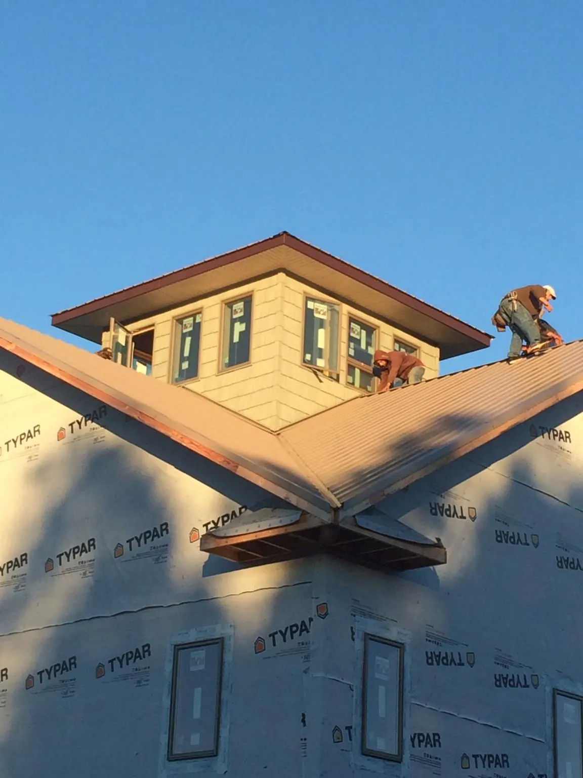 Roofers working around a rooftop cupola on a new metal roof at sunset in Alverton